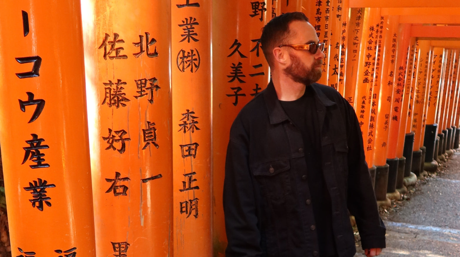 Man standing in front of orange torii gates with Japanese text